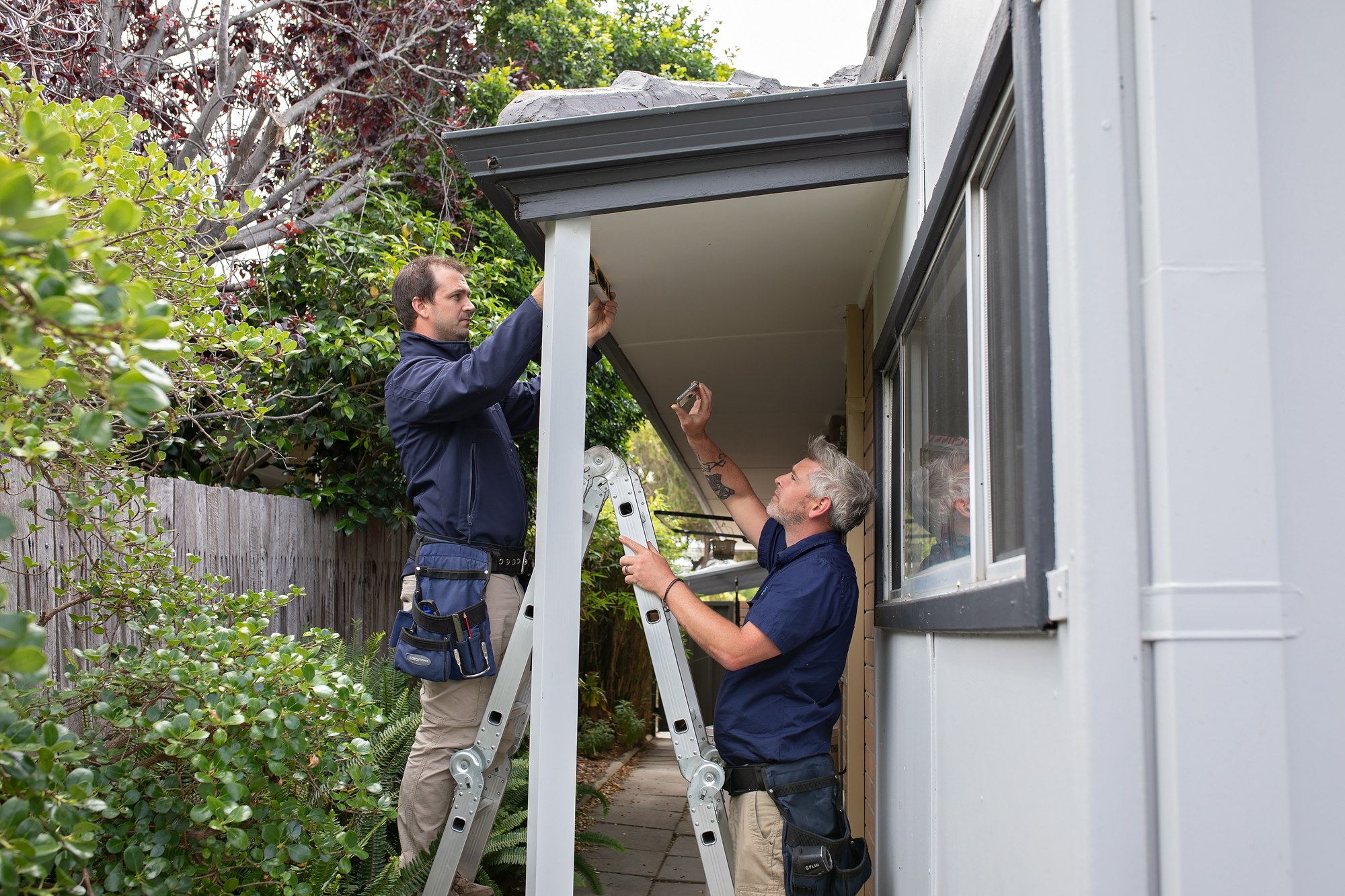 Two inspectors on a ladder checking eaves and fascia