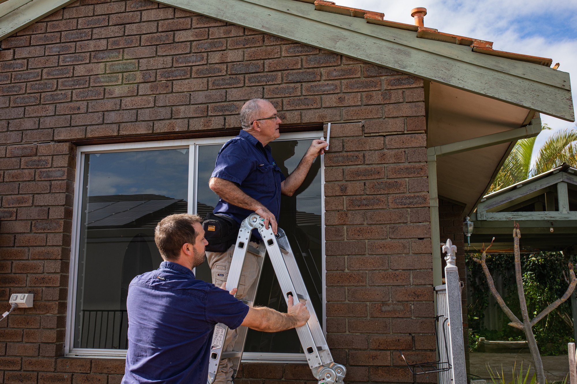 Two SURE inspectors examine brickwork above a window from a ladder