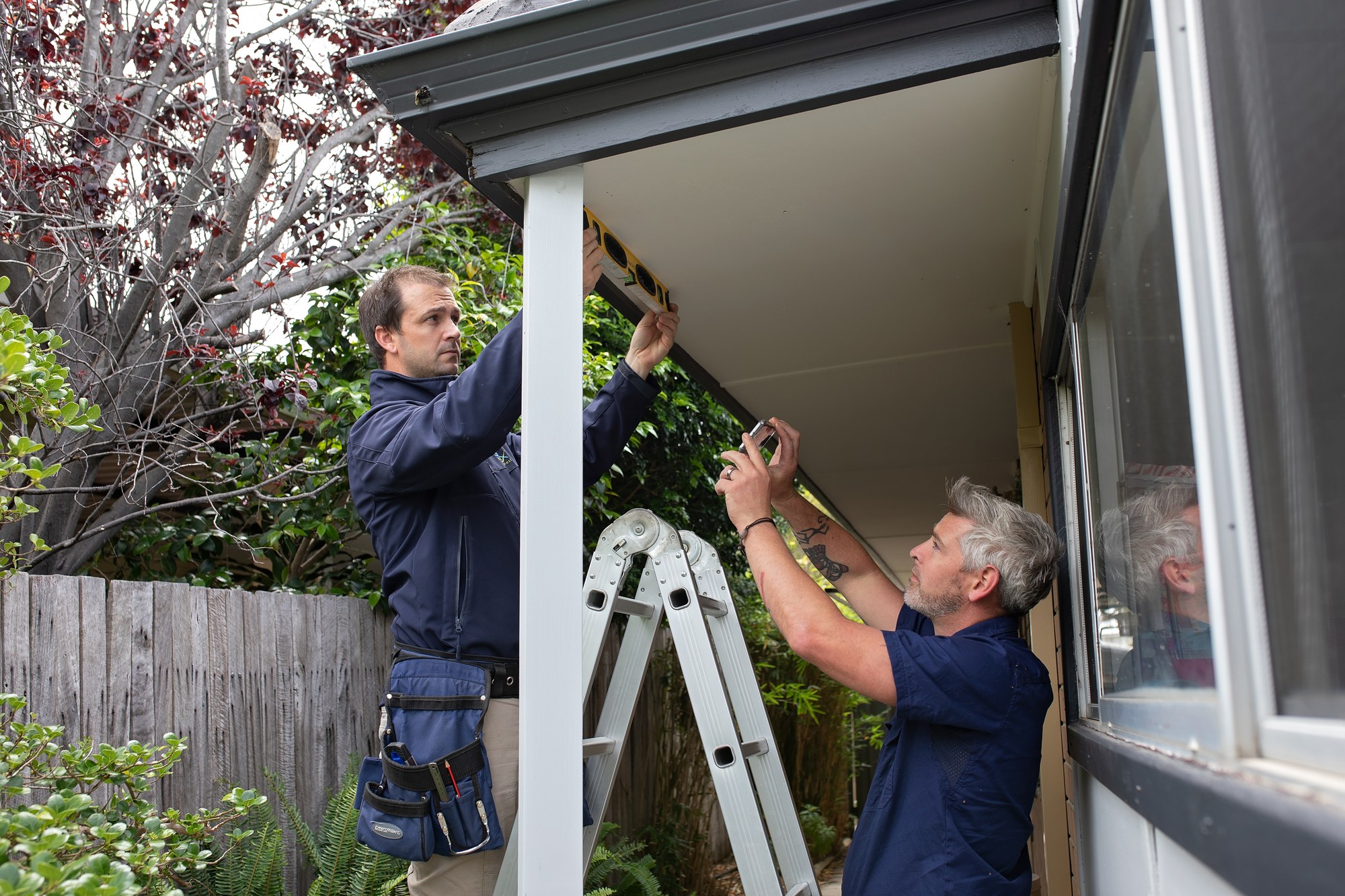 Two SURE inspectors checking eaves with a level and phone camera